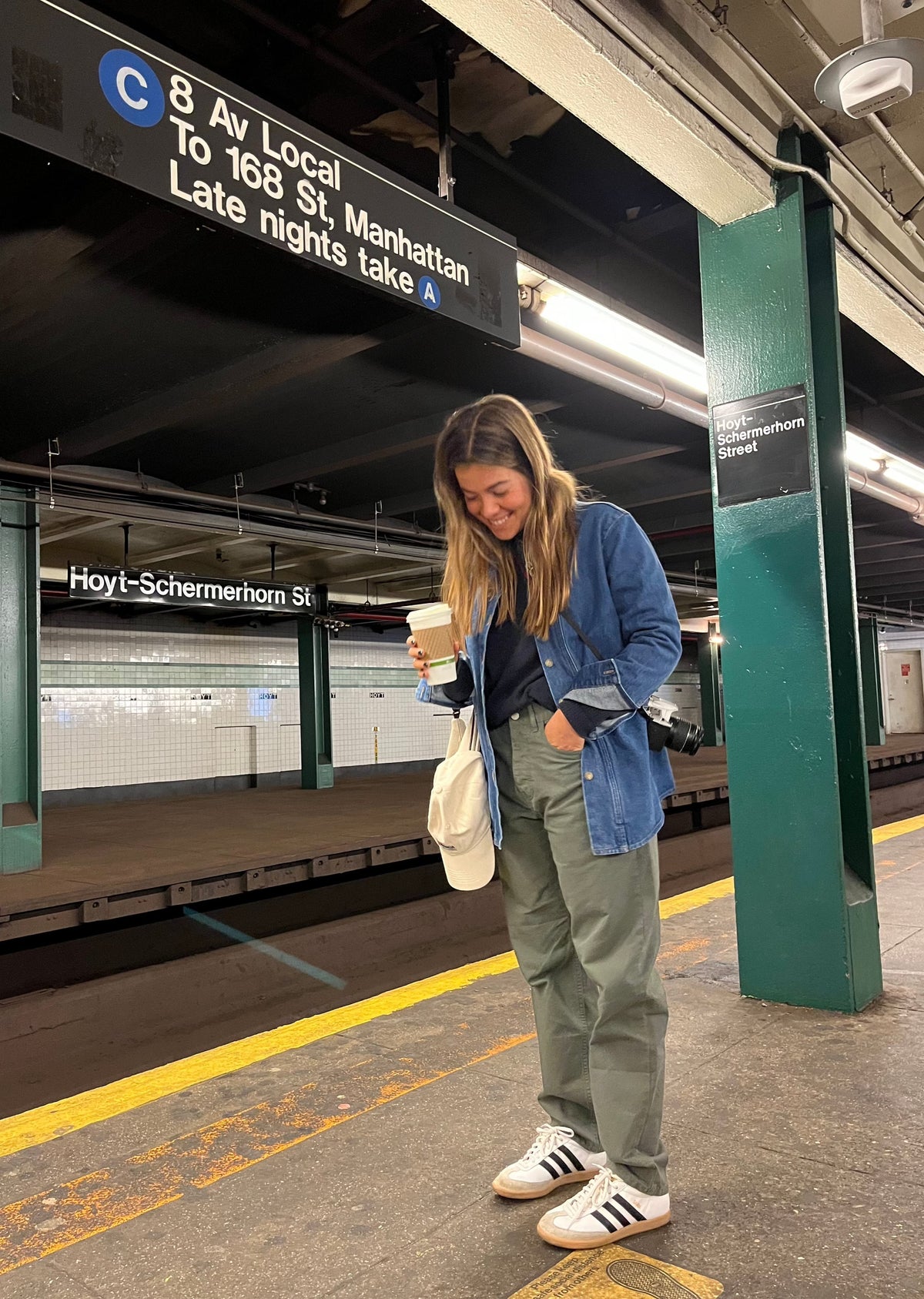 Chica con chaqueta vaquera y un café en el andén de la estación Hoyt-Schermerhorn del metro de Nueva York